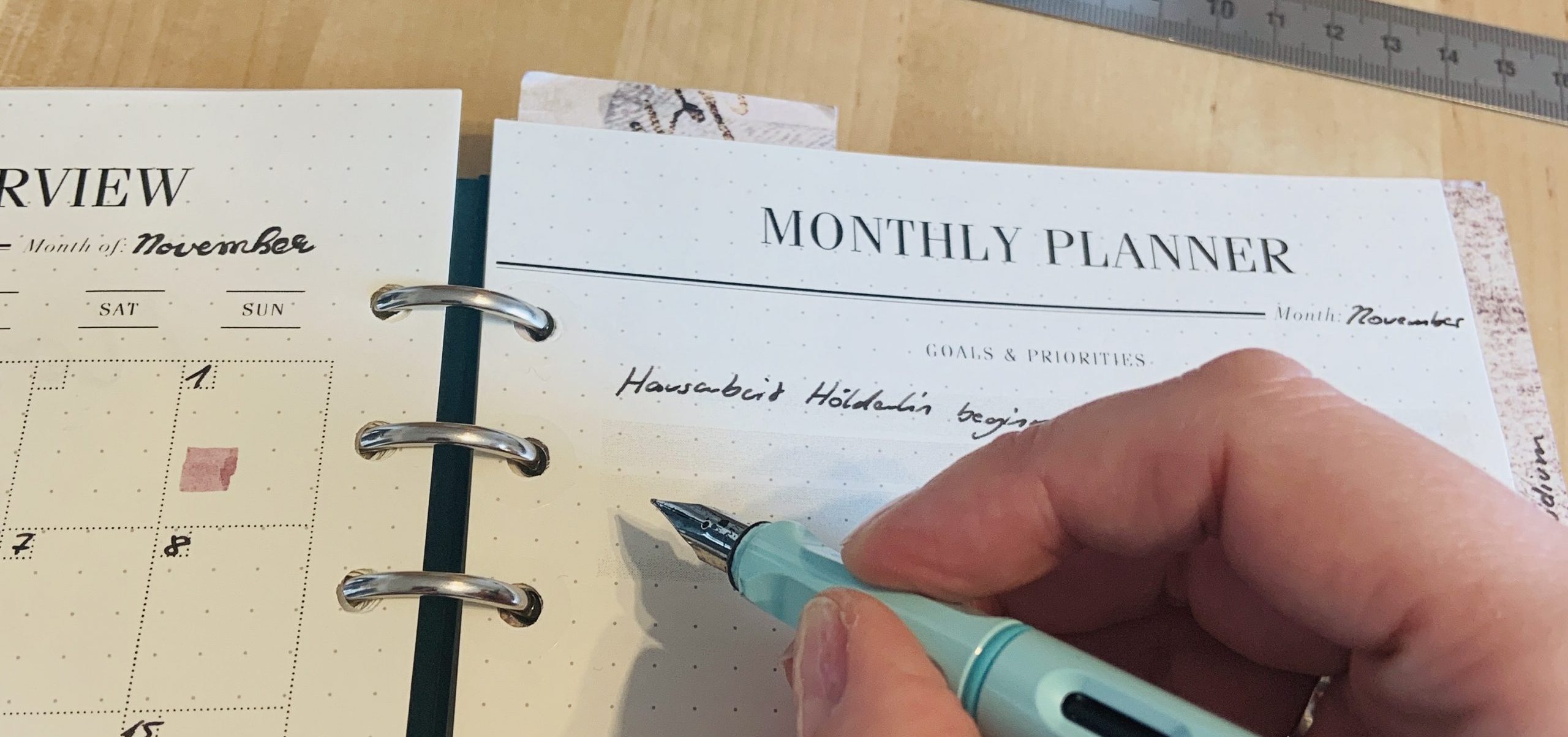 Darstellung eins Monthly Planers im Ringbuch Filofax Clipbook: Hand schreibt mit Füller etwas auf ein Blatt Papier